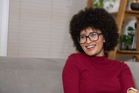 African american woman smiling on sofa wearing glasses in cozy home interior lifestyle