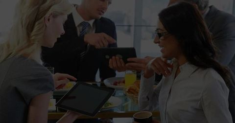 Business team having breakfast meeting with tablets, coffee, fruit in modern daylight office