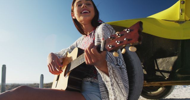 Happy caucasian woman sitting in beach buggy by the sea playing guitar. beach stop off on summer holiday road trip.