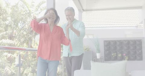 Senior couple enjoying surprise balcony dance while woman covers eyes and partner guides