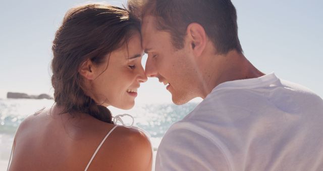 A young Caucasian couple enjoys a romantic moment on a sunny beach, with copy space. Their close embrace and affectionate gaze capture a sense of intimacy and love.