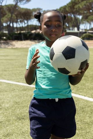 African american girl holding soccer ball on turf during sunny youth sports practice