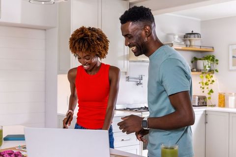African american couple laughing while using laptop on kitchen island with measuring tape