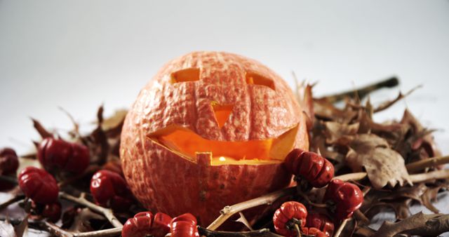 A carved pumpkin sits amidst autumn leaves and berries, signaling the celebration of Halloween. Its glowing face adds a spooky yet festive touch to the seasonal decor.