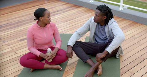 African American Friends Sitting on Rooftop Yoga Mats Talking After Workout Hydrating