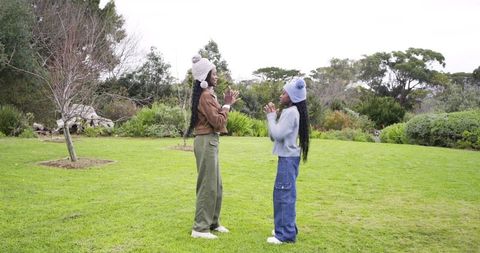 African american girls playing hand-clap game on park lawn wearing knit pom-pom hats