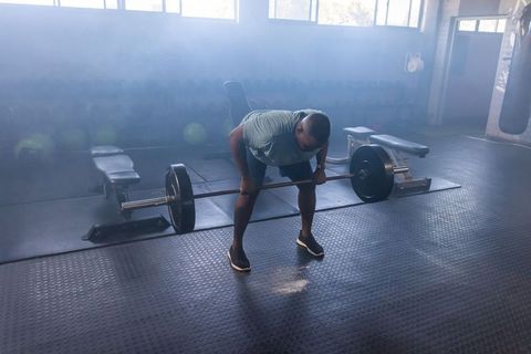 African man preparing to lift loaded barbell in gym performing bent-over rows for strength