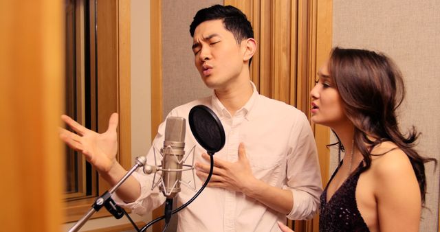 Two singers passionately performing in a professional recording studio. The man is putting hand on his chest while singing into a microphone, while the woman joins in harmony. Suitable for themes related to music production, duets, artist collaboration, audio recording, and creative performances.