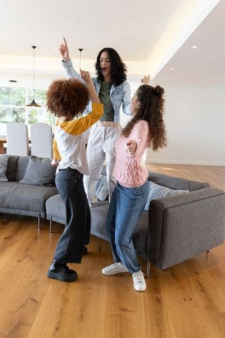 Mother and daughters dancing and singing on sectional sofa in joyful family moment