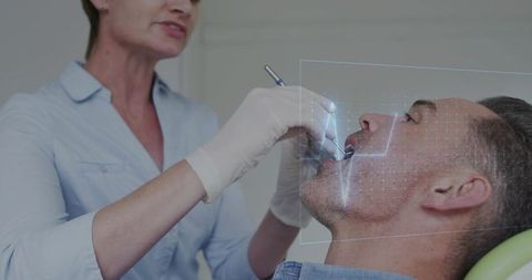 Female dentist examining male patient with digital facial scan overlay during treatment