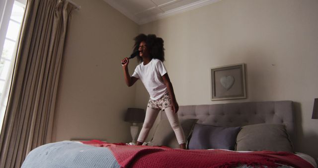 African american girl with hairbrush singing while standing on the bed at home. fatherhood parenthood concept.