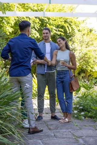Young couple greeting host with clipboard under sunlit pergola in lush garden walkway