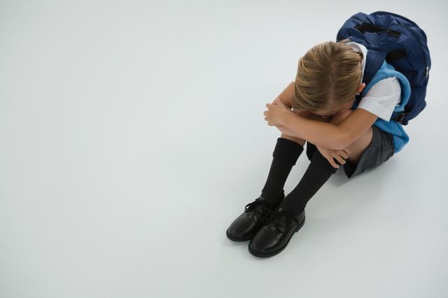 Overhead view of sad schoolboy sitting on white background