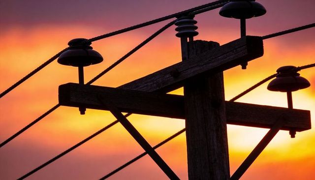 Sunset silhouette of weathered wooden utility pole and power lines, vibrant orange sky