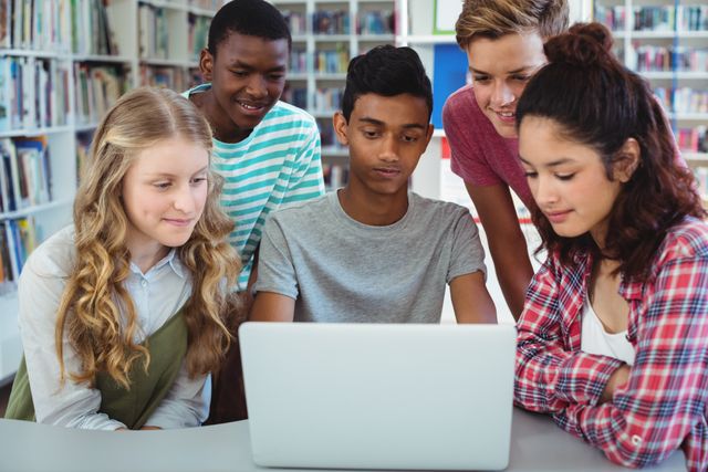 A diverse group of high school students focuses on a laptop screen while working together in a library. This image can be used for educational content, promoting teamwork and collaboration, school projects, or advertisements related to technology in education.