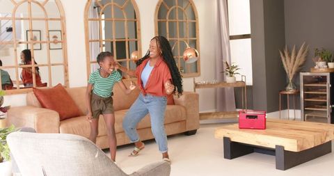 African american mother and teen daughter dancing in sunlit living room with retro speaker