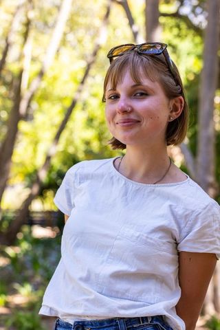 Young woman smiling in sunlit park wearing white tee, denim jeans, sunglasses on head