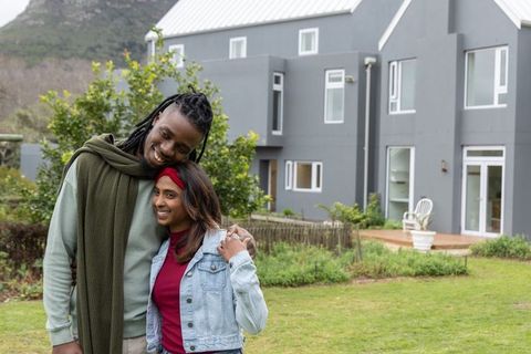 Couple embracing on lawn outside modern gray home, smiling and relaxing together