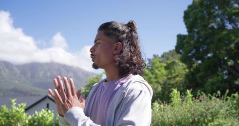 African man standing and practicing meditation in lakeside garden with mountain view