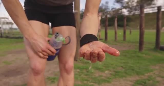 Woman washing hands with water from bottle after a challenging bootcamp session at an outdoor fitness gym, showing dedication to post-workout hygiene. Great for advertising sports gear, fitness programs, health and wellness products, and demonstrating commitment to good hygiene practices.