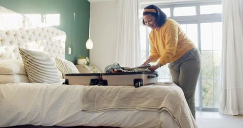 Woman Packing Suitcase on Comfortable Hotel Bed in Sunlit Room