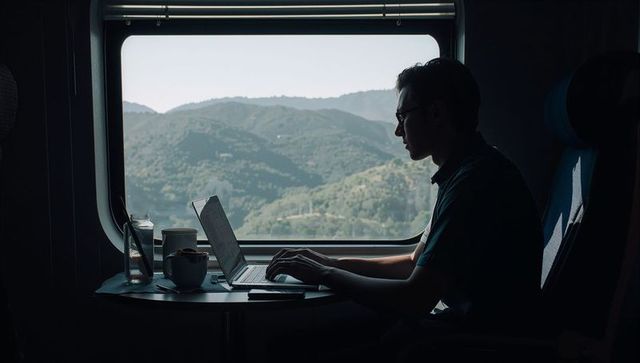 Working commuter typing on laptop at train window with scenic mountain landscape