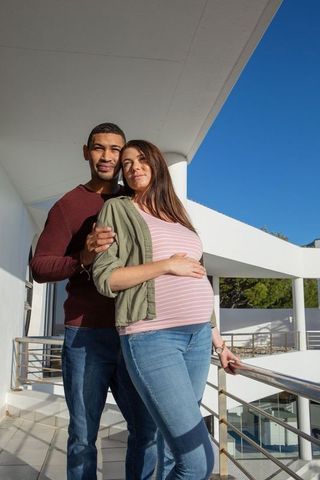 Diverse Couple Embrace on Balcony Safeguarded by Metal Railing
