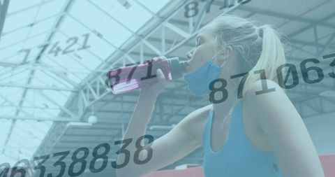Woman wearing face mask drinking water in gym