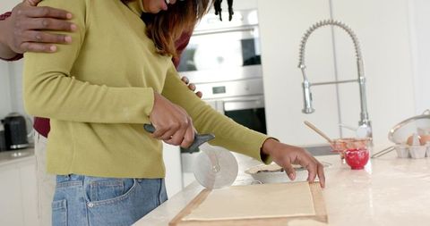 Diverse couple baking together embracing while man guiding woman cutting pastry dough