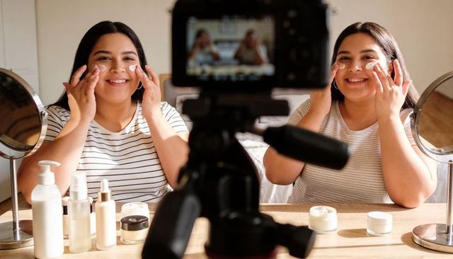Smiling beauty duo filming skincare routine with creams, mirrors, camera on tripod