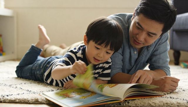 Father and son reading picture book on living room rug sharing cozy home storytime