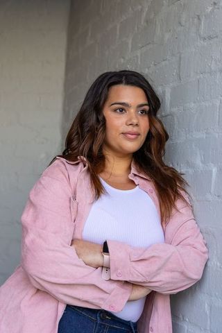 Thoughtful woman leaning against brick wall wearing pink shirt and smartwatch