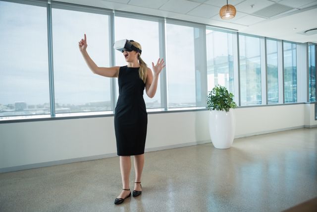 Young female executive engaging with virtual reality headset in a modern office environment. Ideal for illustrating concepts of innovation, technology in the workplace, and the future of business. Suitable for use in articles, presentations, and marketing materials related to corporate technology, VR applications, and professional settings.