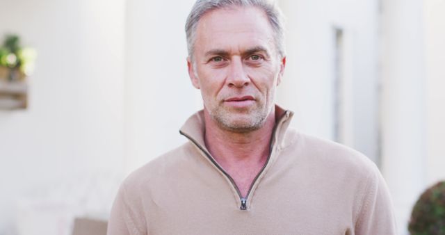 Middle-aged man with grey hair wearing a beige casual top, smiling confidently outdoors in natural light. This image is ideal for use in advertisements, lifestyle blogs, wellness campaigns, or articles about successful aging.