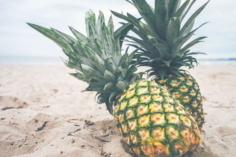Tropical pineapples resting on sandy beach under soft cloudy sky for summer lifestyle
