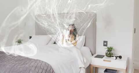 Sunlit minimalist bedroom woman sipping coffee while reading on cozy white bed with tablet