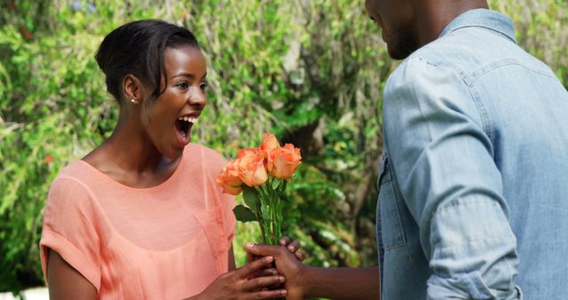 A woman is expressing joy and surprise as a man hands her a bouquet of orange flowers. Use this image to illustrate friendship, gift-giving, expressions of happiness, and positive outdoor interactions.