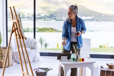 Senior asian artist painting in sunlit waterfront studio with easel and brushes
