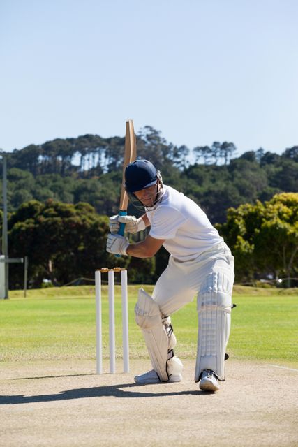 Cricket player in action, batting on a well-maintained field under a clear sky. Ideal for use in sports magazines, cricket event promotions, athletic training materials, and outdoor activity advertisements.
