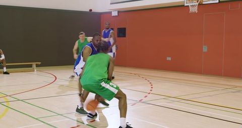 Guard dribbling and driving past defender while teammate preparing jump shot on indoor court