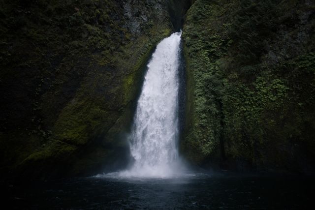 Majestic scene depicting a powerful waterfall cascading through a moss-covered rock formation. Ideal for use in travel brochures, nature documentaries, environmental awareness campaigns, and as a calming landscape background.