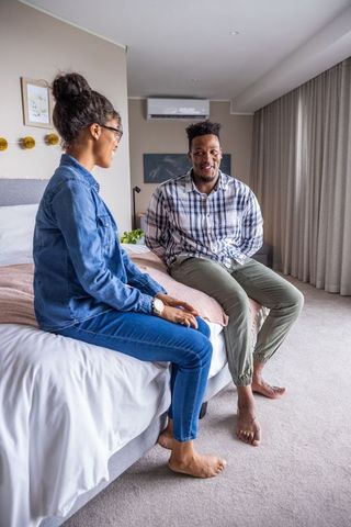 Couple sitting on bed edge having intimate conversation in cozy modern bedroom
