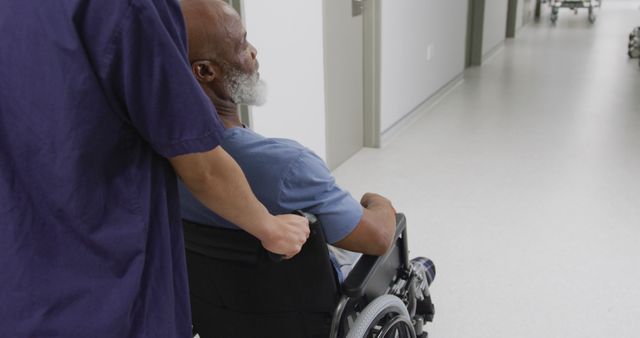 Diverse female doctor pushing senior male patient in wheelchair down hospital corridor. Medicine, healthcare, lifestyle and hospital concept.