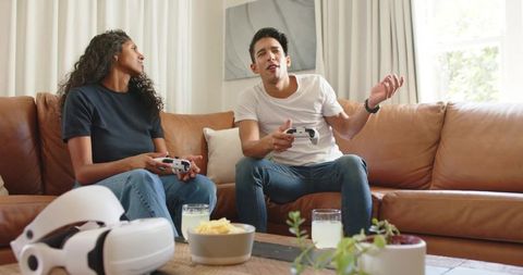 Young couple playing console games on leather couch with controllers and vr headset casual