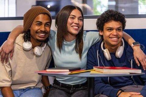 Smiling diverse students studying together in college lounge wearing headphones