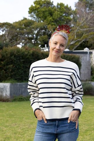 Mature woman wearing merry christmas headband and striped sweater standing in garden portrait