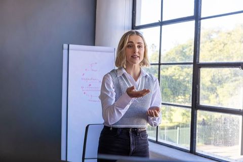 Female professional presenting training with flip chart by large industrial window in daylight