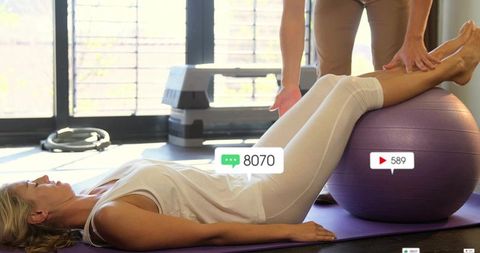 Woman doing leg raises on stability ball with trainer assisting for core rehab workout