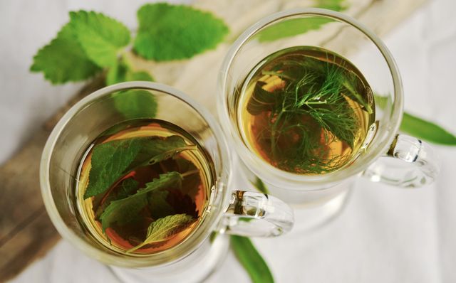Two glass cups filled with herbal tea containing fresh mint and dill leaves. Perfect for uses in articles, blogs, or advertisements focused on health, wellness, organic living, and herbal remedies. Great for illustrating recipes for a refreshing and healthy drink.