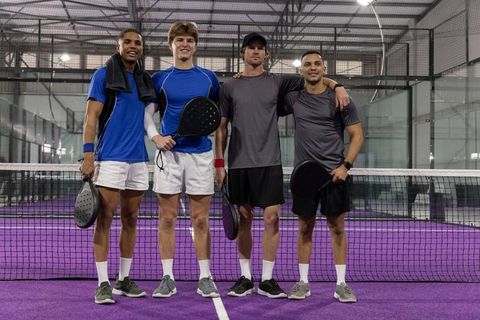 Male padel teammates posing on purple indoor court holding black paddles showing team unity